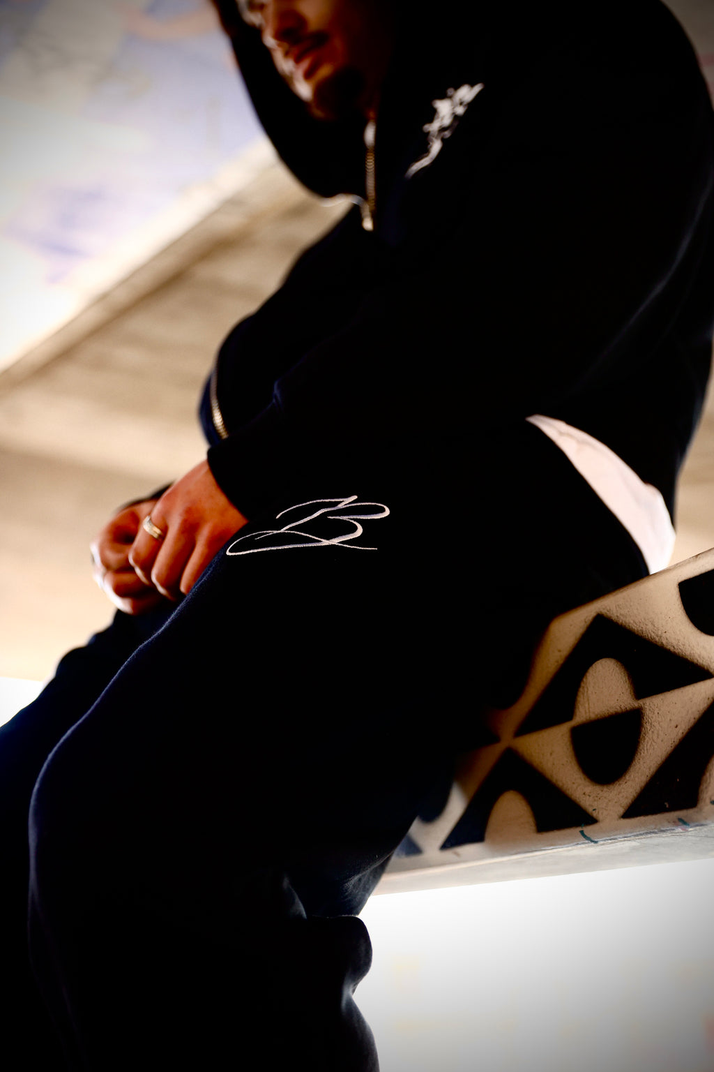 Person wearing joggers and hoodie with branding siting on a railing