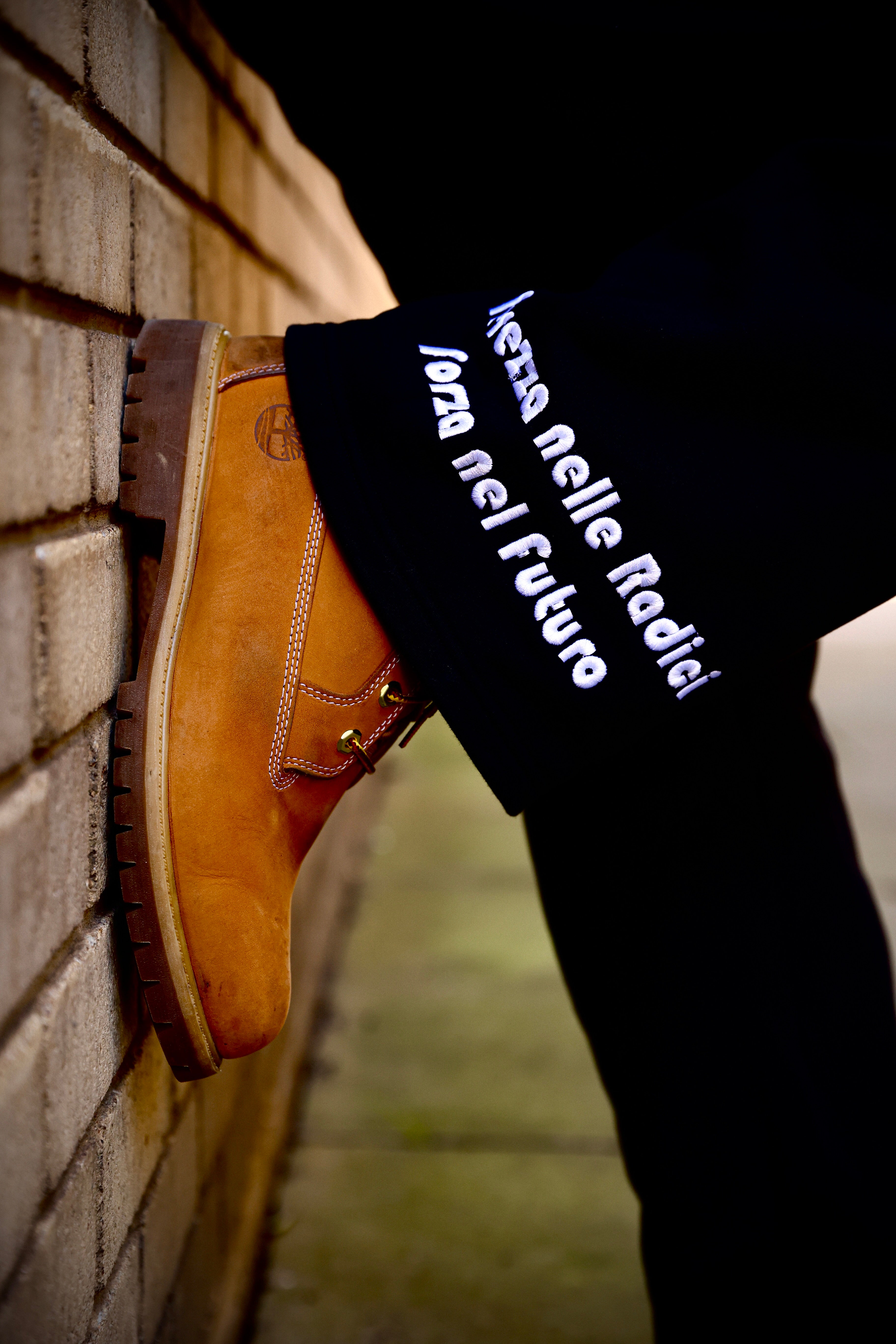 Brown leather shoe leaning against a brick wall with text on a black sock.