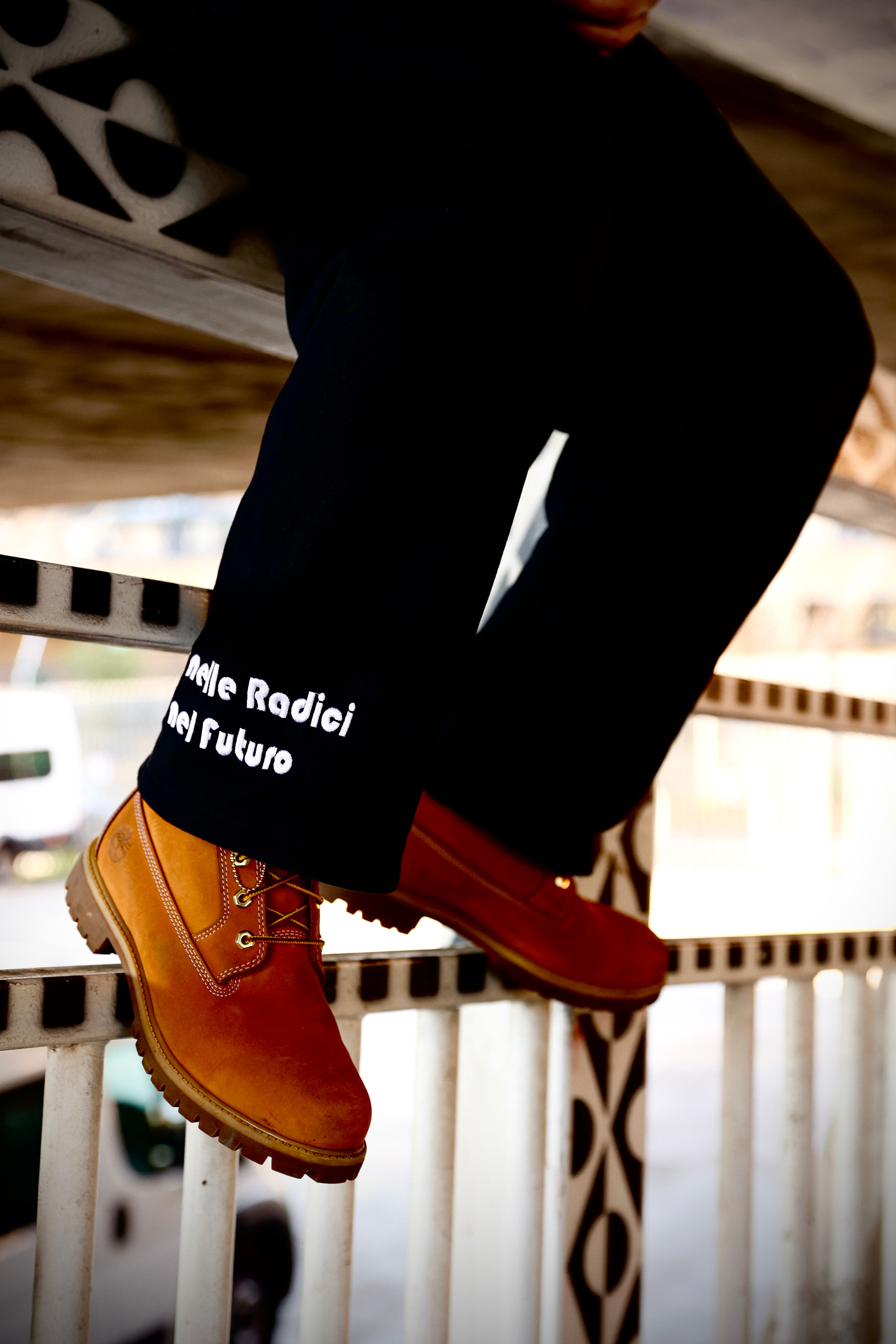 Person wearing brown boots and black pants with text, sitting on a railing.